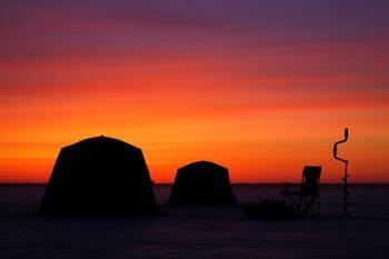 Силуэты палаток и рыбаков на льду на фоне заката