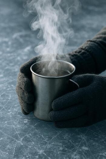 Руки рыбака держат кружку с паром на фоне зимнего льда