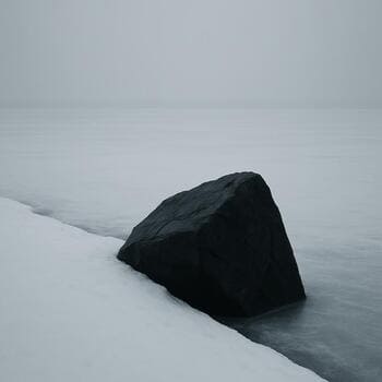 Один крупный камень выделяется на заснеженной береговой линии