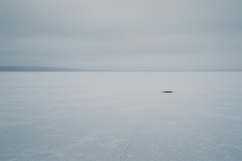 Одна лунка и рыболов на большом открытом льду вдали от лагеря
